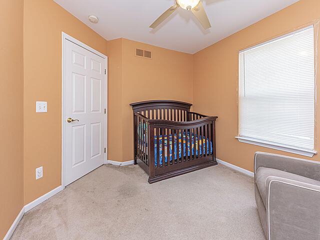 bedroom featuring a nursery area, light colored carpet, and ceiling fan