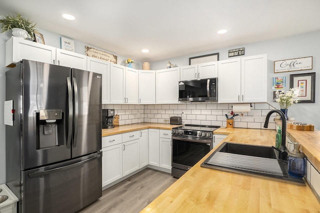 kitchen featuring butcher block counters, tasteful backsplash, light hardwood / wood-style flooring, appliances with stainless steel finishes, and white cabinets