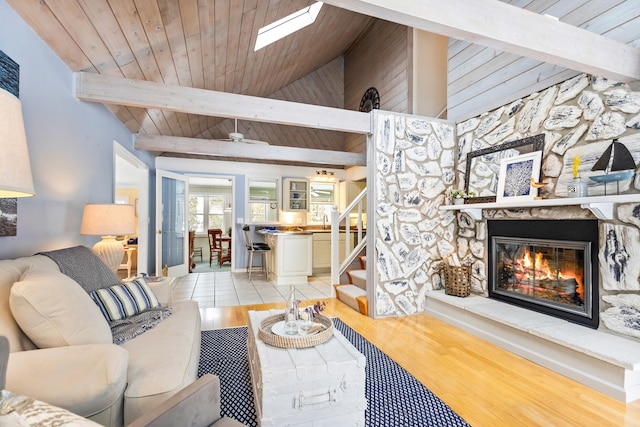 living room with light wood-style flooring, stairway, lofted ceiling with beams, a stone fireplace, and wood ceiling