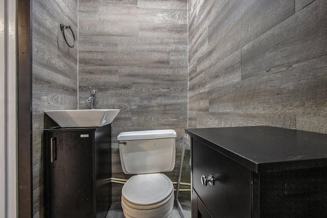 bathroom featuring toilet, sink, and wood walls