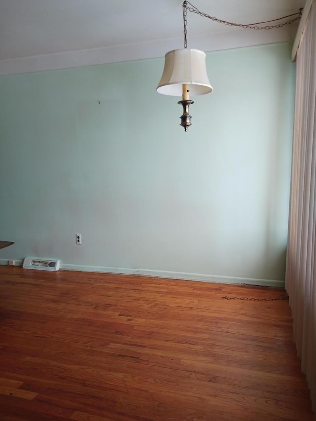 empty room with baseboards, visible vents, and wood finished floors