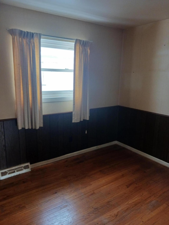 spare room featuring wood-type flooring, visible vents, and baseboards