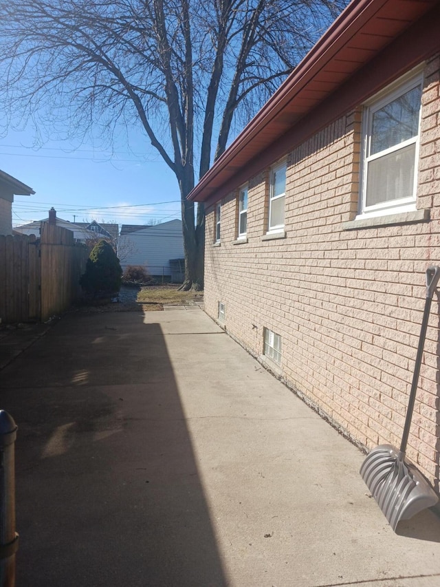 view of side of home with a patio area, fence, and brick siding