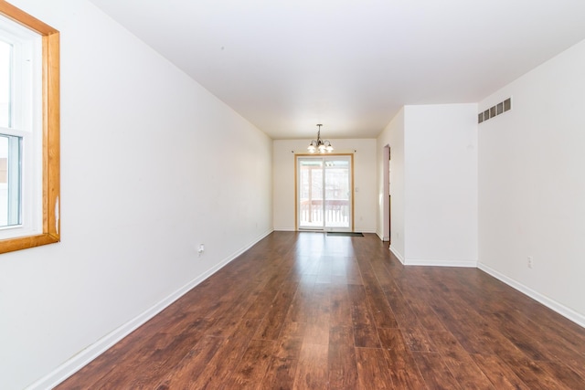 unfurnished room featuring dark wood-type flooring and an inviting chandelier