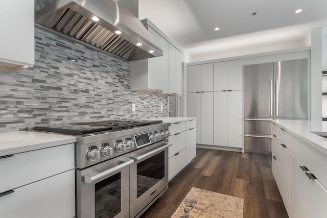 kitchen with tasteful backsplash, white cabinetry, stainless steel appliances, dark wood-type flooring, and wall chimney exhaust hood