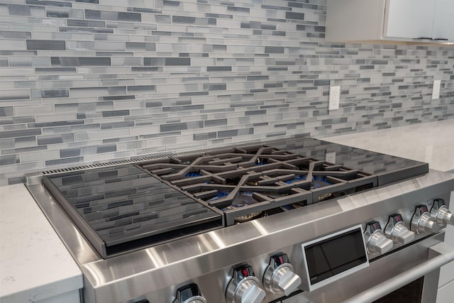 room details featuring tasteful backsplash, stainless steel gas range, and white cabinets