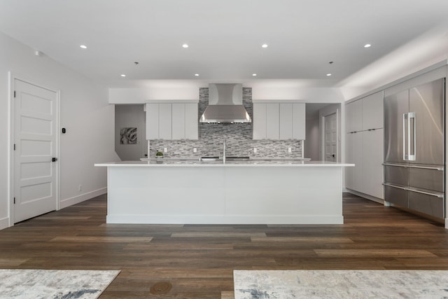 kitchen featuring an island with sink, sink, backsplash, dark wood-type flooring, and wall chimney exhaust hood