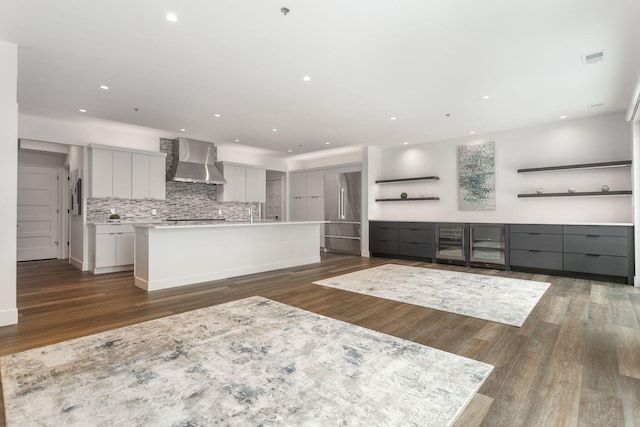 kitchen with wall chimney range hood, dark wood-type flooring, gray cabinetry, backsplash, and a spacious island