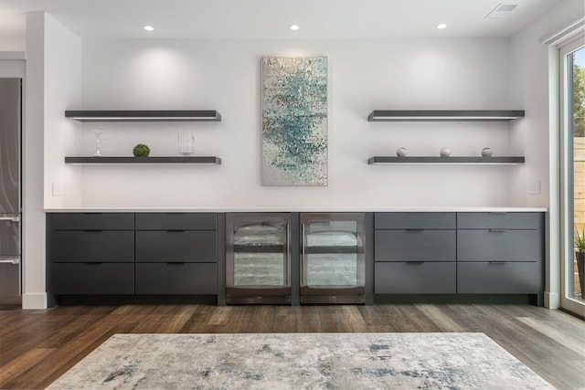 bar with stainless steel refrigerator, gray cabinetry, beverage cooler, and dark hardwood / wood-style flooring