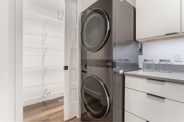 laundry room featuring cabinets, stacked washing maching and dryer, and light hardwood / wood-style floors