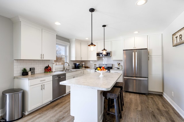 kitchen with a kitchen island, appliances with stainless steel finishes, pendant lighting, white cabinetry, and backsplash