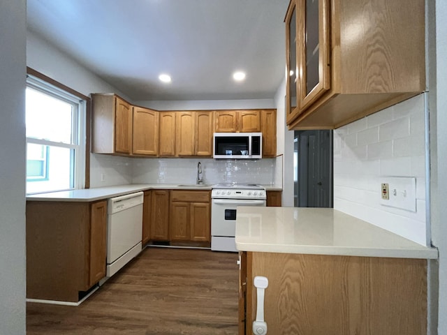 kitchen featuring sink, white appliances, dark wood-type flooring, decorative backsplash, and kitchen peninsula