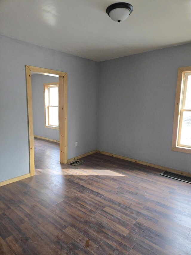 empty room featuring dark wood-style flooring, visible vents, and baseboards