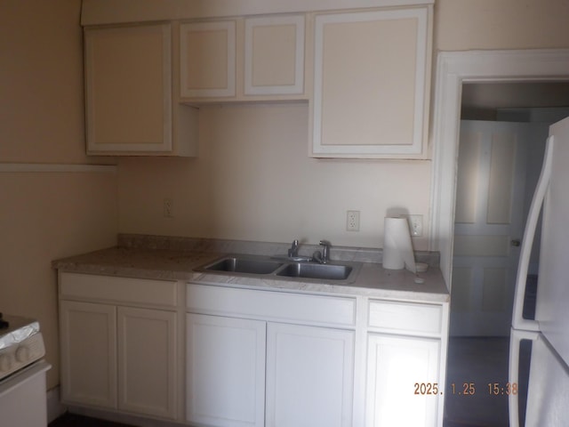 kitchen with stove, sink, white cabinets, and white fridge