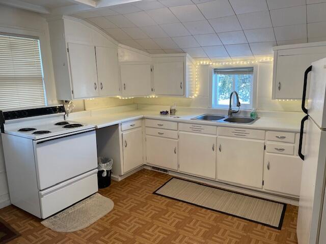 kitchen with sink, white appliances, light parquet floors, and white cabinets