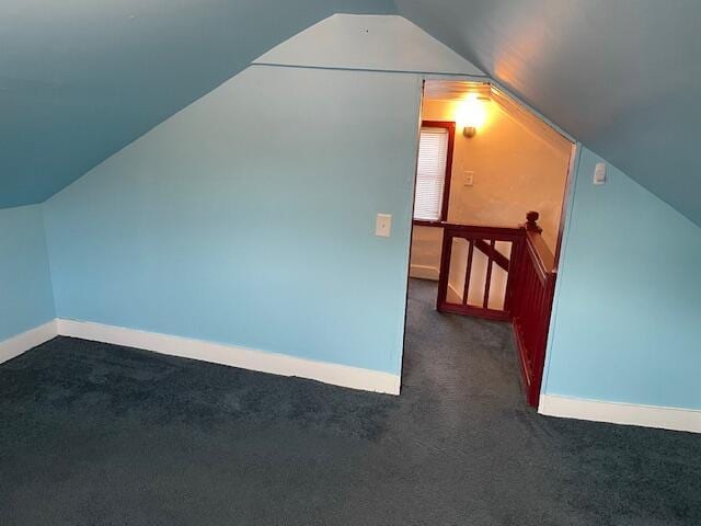 additional living space featuring dark colored carpet and lofted ceiling