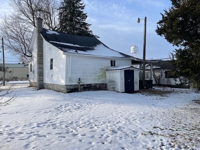 snow covered rear of property featuring a shed