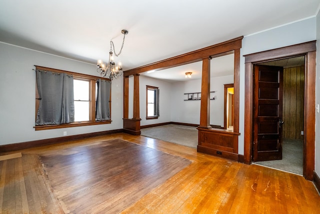 spare room featuring a notable chandelier, hardwood / wood-style floors, and ornate columns