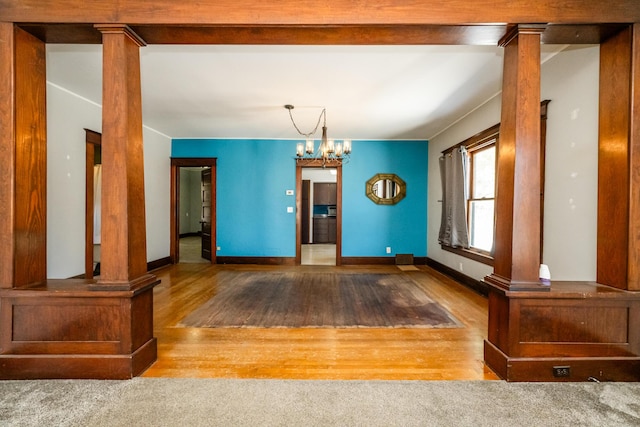 unfurnished dining area featuring light hardwood / wood-style floors, a chandelier, and decorative columns