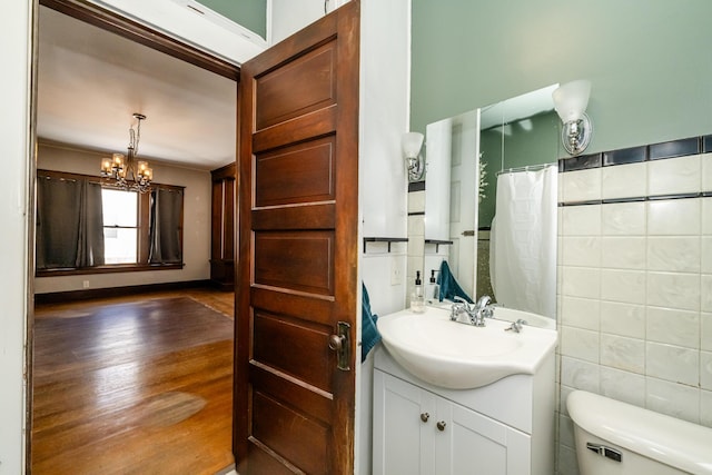 bathroom with tile walls, hardwood / wood-style flooring, vanity, a notable chandelier, and toilet