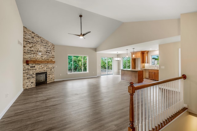 unfurnished living room featuring a stone fireplace, ceiling fan with notable chandelier, high vaulted ceiling, and hardwood / wood-style flooring