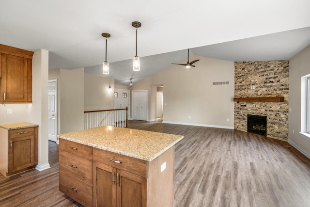 kitchen with a kitchen island, dark hardwood / wood-style floors, a fireplace, lofted ceiling, and light stone counters