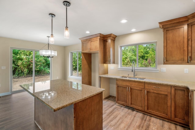 kitchen with a kitchen island, pendant lighting, sink, light stone countertops, and light wood-type flooring