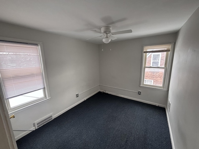 empty room with ceiling fan and dark colored carpet