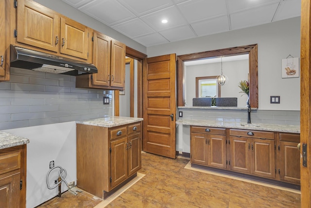 kitchen featuring pendant lighting, decorative backsplash, and light stone countertops