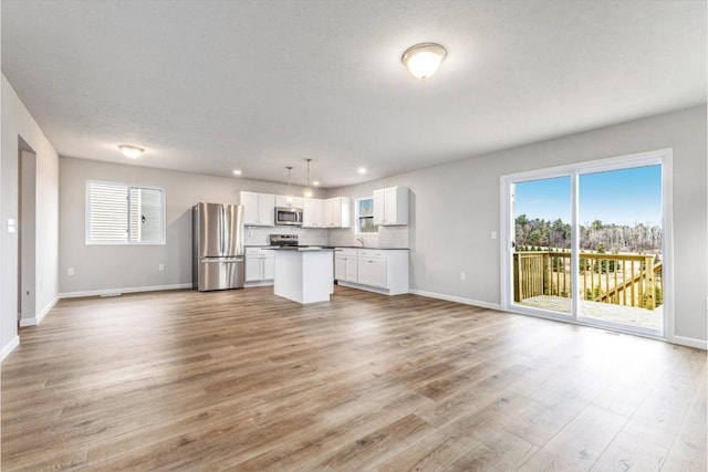 kitchen featuring light hardwood / wood-style flooring, hanging light fixtures, appliances with stainless steel finishes, a kitchen island, and white cabinets