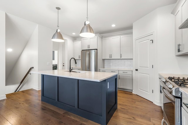 kitchen with sink, light stone counters, hanging light fixtures, a center island with sink, and stainless steel appliances