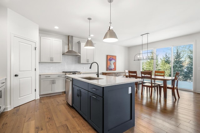 kitchen featuring sink, decorative light fixtures, a center island with sink, wall chimney range hood, and white cabinets