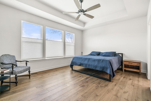 bedroom featuring ceiling fan, a tray ceiling, and light wood-type flooring