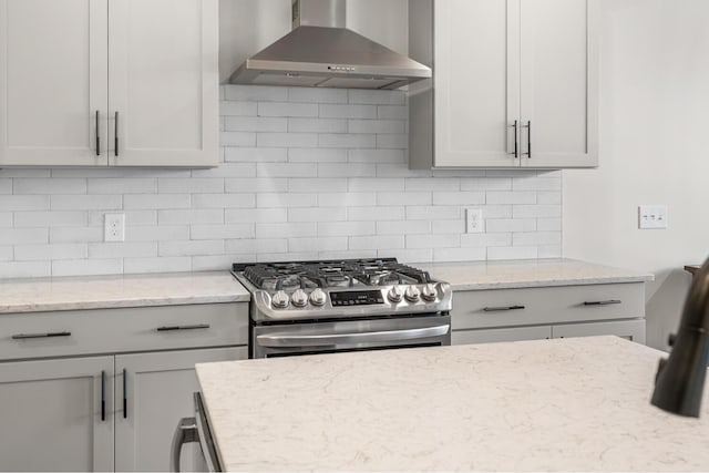 kitchen with light stone counters, wall chimney range hood, backsplash, and gas stove