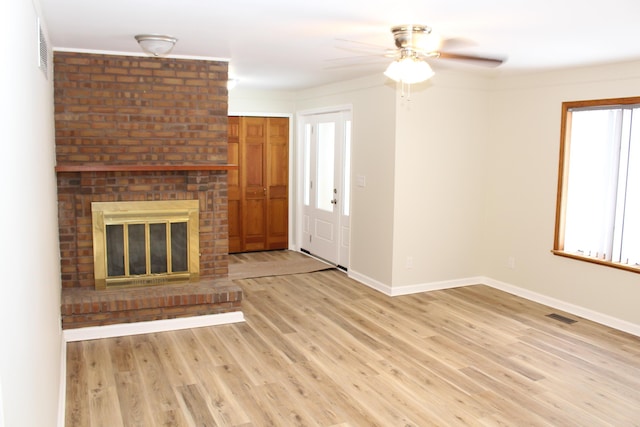 unfurnished living room with ceiling fan, a brick fireplace, and light wood-type flooring