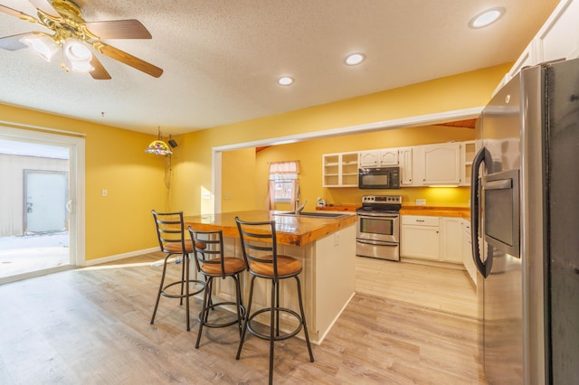 kitchen featuring a breakfast bar, wood counters, white cabinetry, sink, and stainless steel appliances