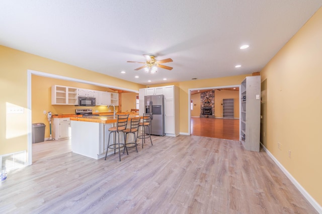 kitchen with appliances with stainless steel finishes, a kitchen breakfast bar, ceiling fan, light hardwood / wood-style floors, and white cabinets