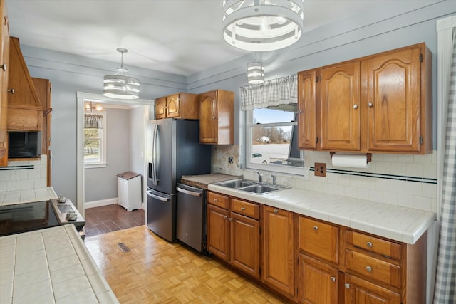 kitchen featuring sink, tasteful backsplash, tile countertops, pendant lighting, and stainless steel appliances