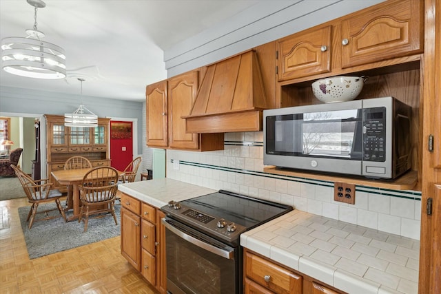 kitchen with decorative backsplash, custom exhaust hood, light parquet floors, tile counters, and stainless steel appliances