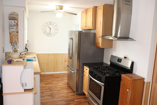 kitchen featuring wooden walls, sink, wall chimney range hood, stainless steel gas range, and light hardwood / wood-style flooring