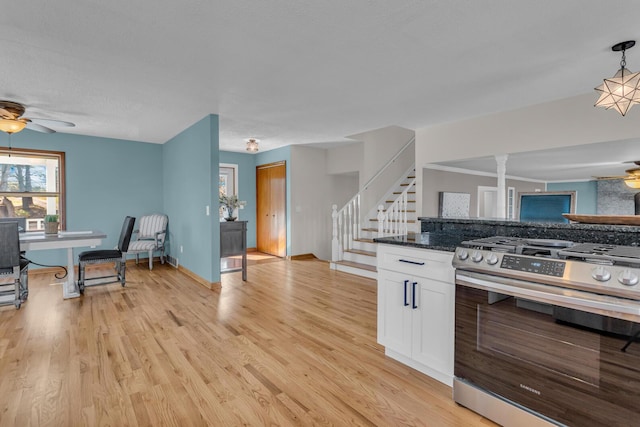 kitchen featuring dark stone countertops, light hardwood / wood-style floors, white cabinets, gas range, and decorative light fixtures