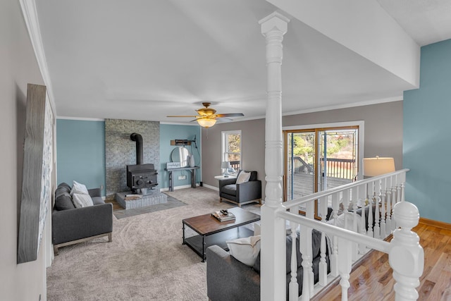 living room with ornate columns, light hardwood / wood-style flooring, a wood stove, ornamental molding, and ceiling fan