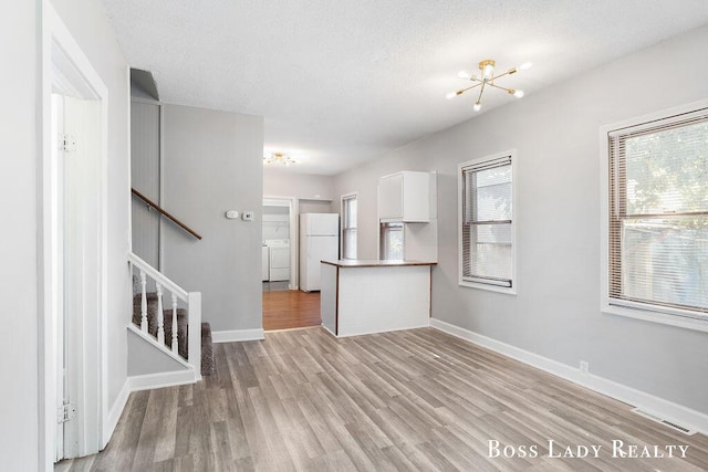 unfurnished living room featuring a chandelier, light hardwood / wood-style floors, a textured ceiling, and washing machine and dryer