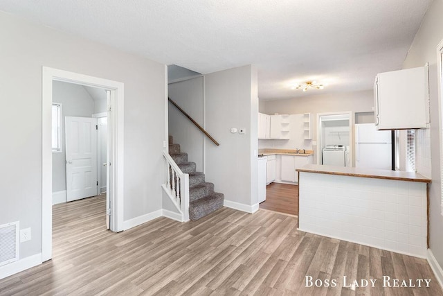 kitchen featuring white cabinetry, white refrigerator, light hardwood / wood-style floors, washer / dryer, and kitchen peninsula