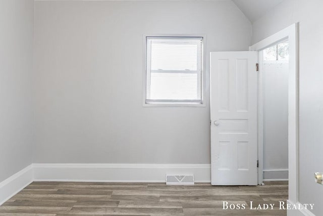 unfurnished room featuring plenty of natural light, vaulted ceiling, and hardwood / wood-style floors