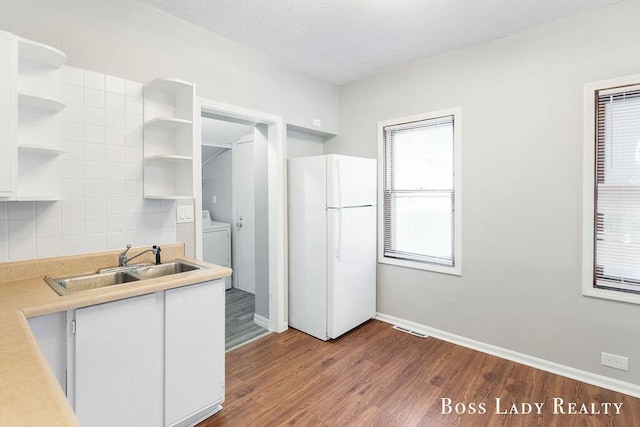 kitchen featuring washing machine and clothes dryer, sink, white fridge, hardwood / wood-style flooring, and white cabinets