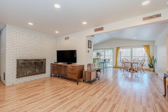 living room featuring a brick fireplace, lofted ceiling, and light hardwood / wood-style flooring