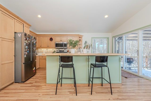 kitchen with stainless steel appliances, light wood-type flooring, a center island with sink, and light brown cabinets