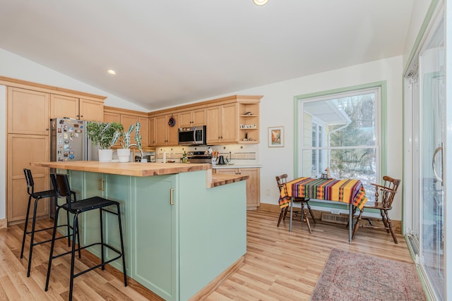 kitchen featuring lofted ceiling, butcher block counters, a center island, light wood-type flooring, and appliances with stainless steel finishes