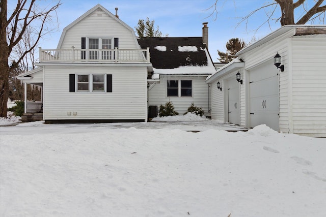 snow covered back of property with a garage and a balcony